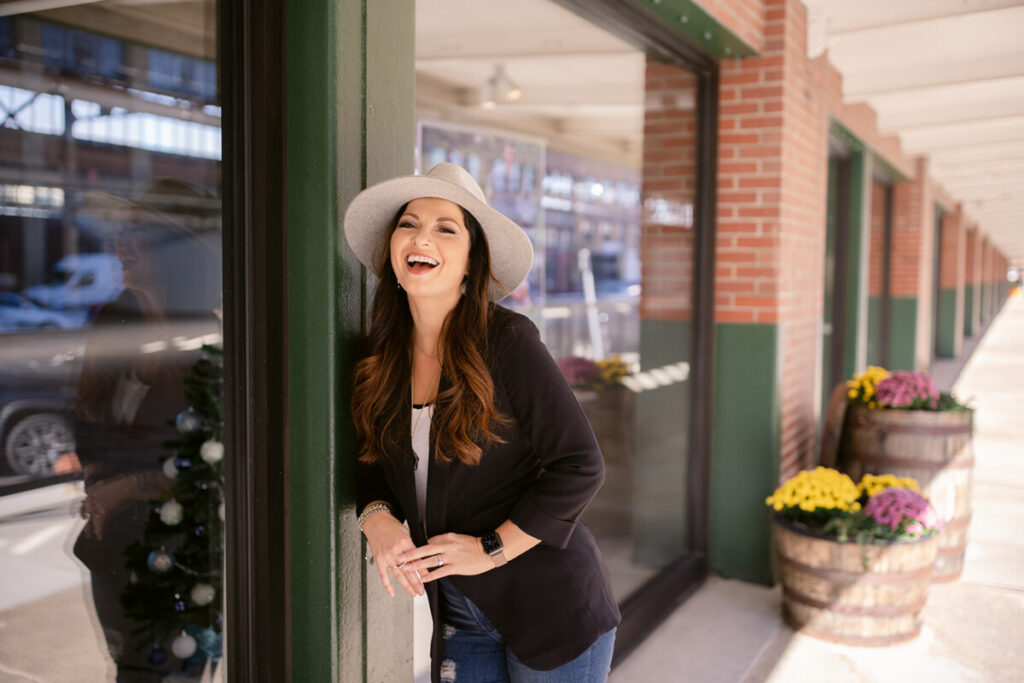 Professional woman smiling while leaning against a wall outdoors, symbolizing overcoming burnout through a nervous system reset. 